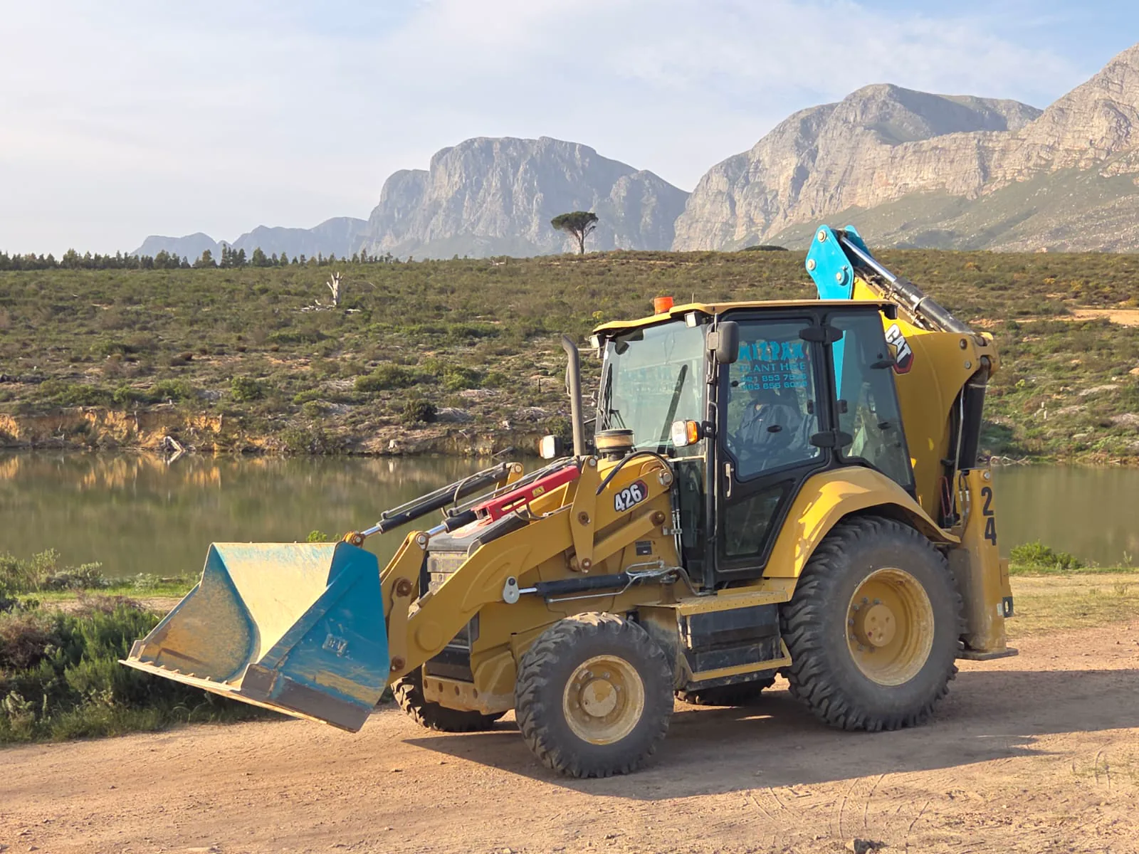 Mizpah Plant Hire TLB beside water with the Helderberg mountains behind it